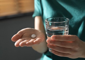 Person with a glass of water and pill in their hand