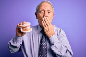 Senior man covering his mouth while holding denture model