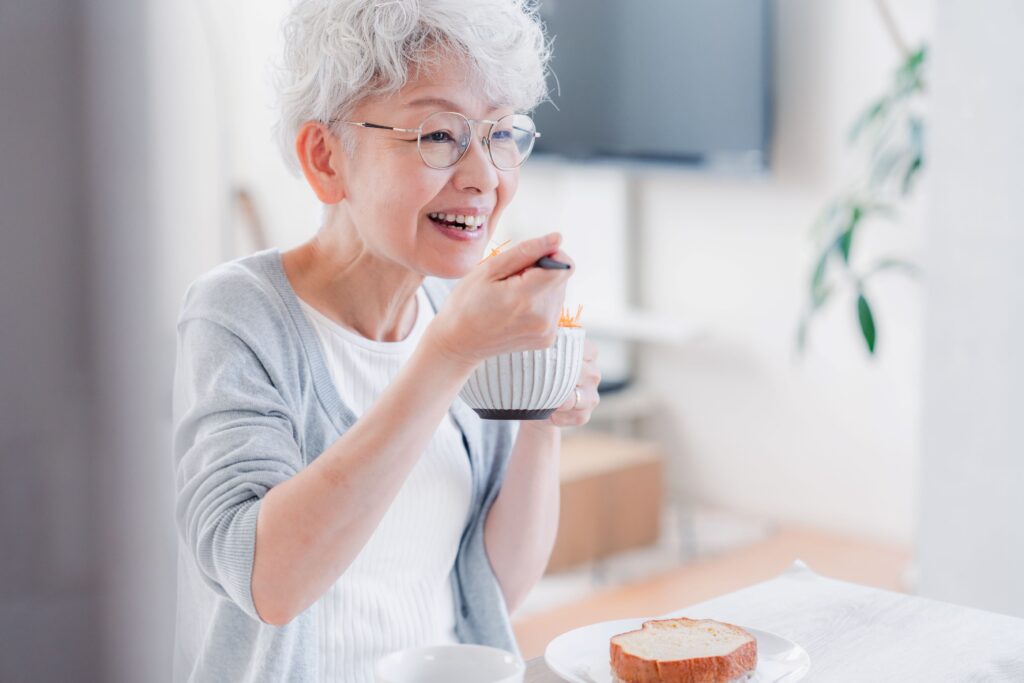 Woman with gray hair eating something from white bowl